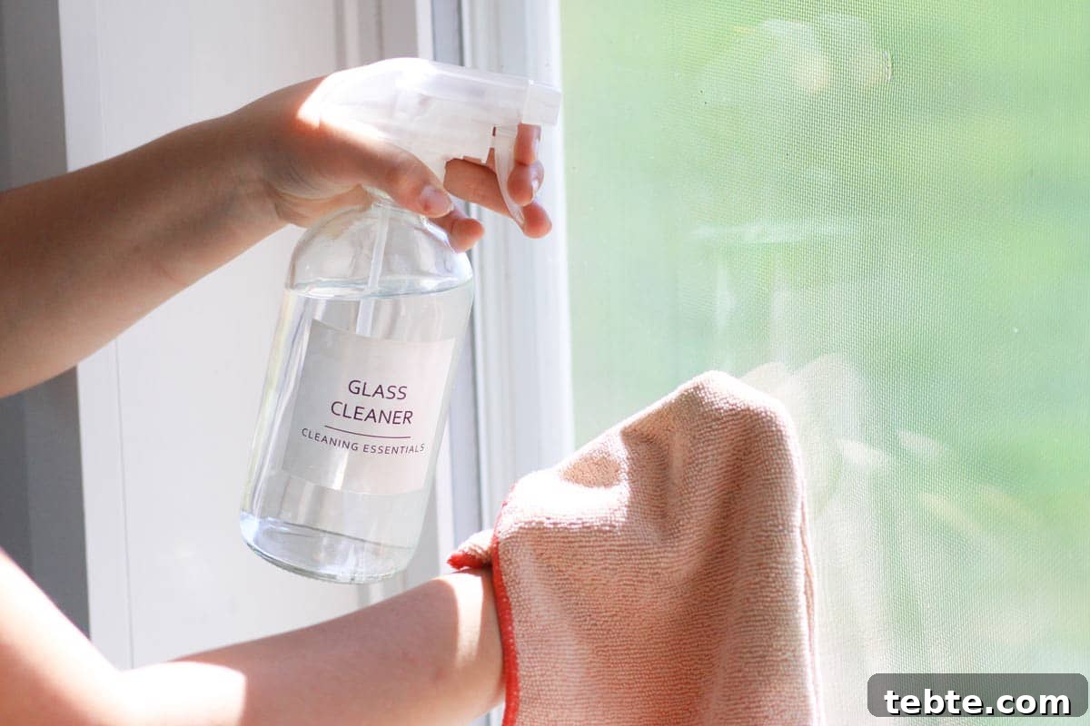 Homemade Non-Toxic Glass Cleaner with Vinegar — DIY Recipe 3 a glass spray bottle with a label that says "glass cleaner with a pink microfiber cloth next to it