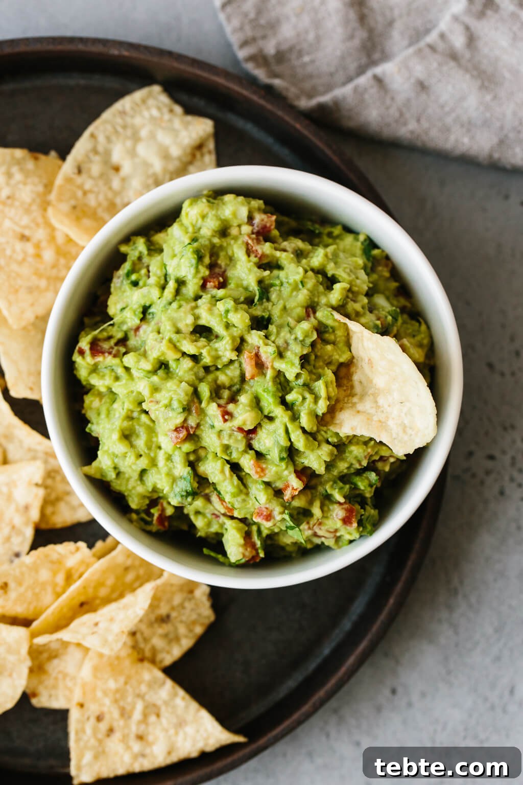 Guacamole in a bowl surrounded by chips. One chip in the guacamole.