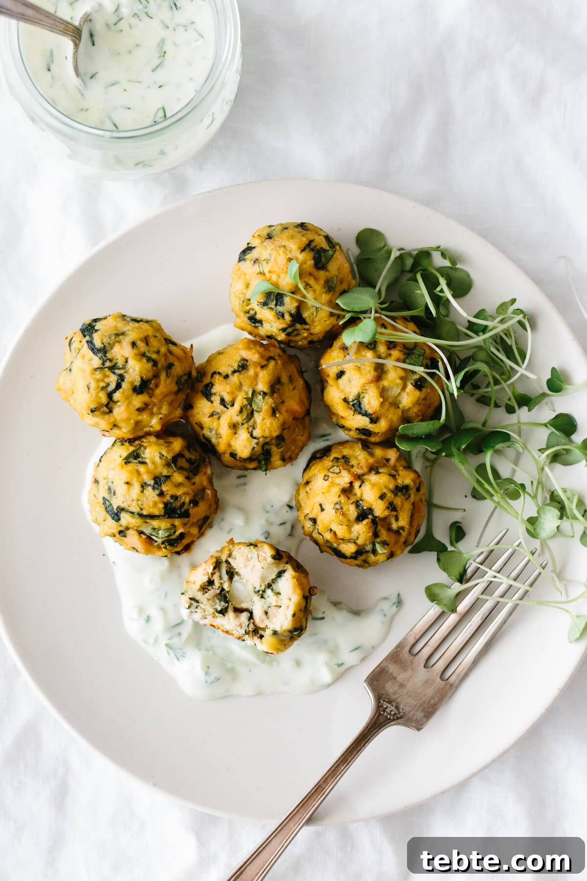 Tuna meatballs on a plate with tzatziki sauce and micro greens.