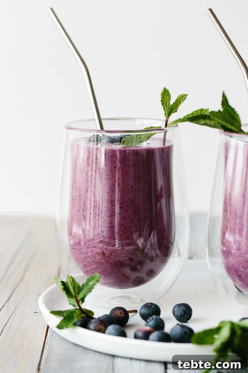 Blueberry smoothie in a glass with straw.