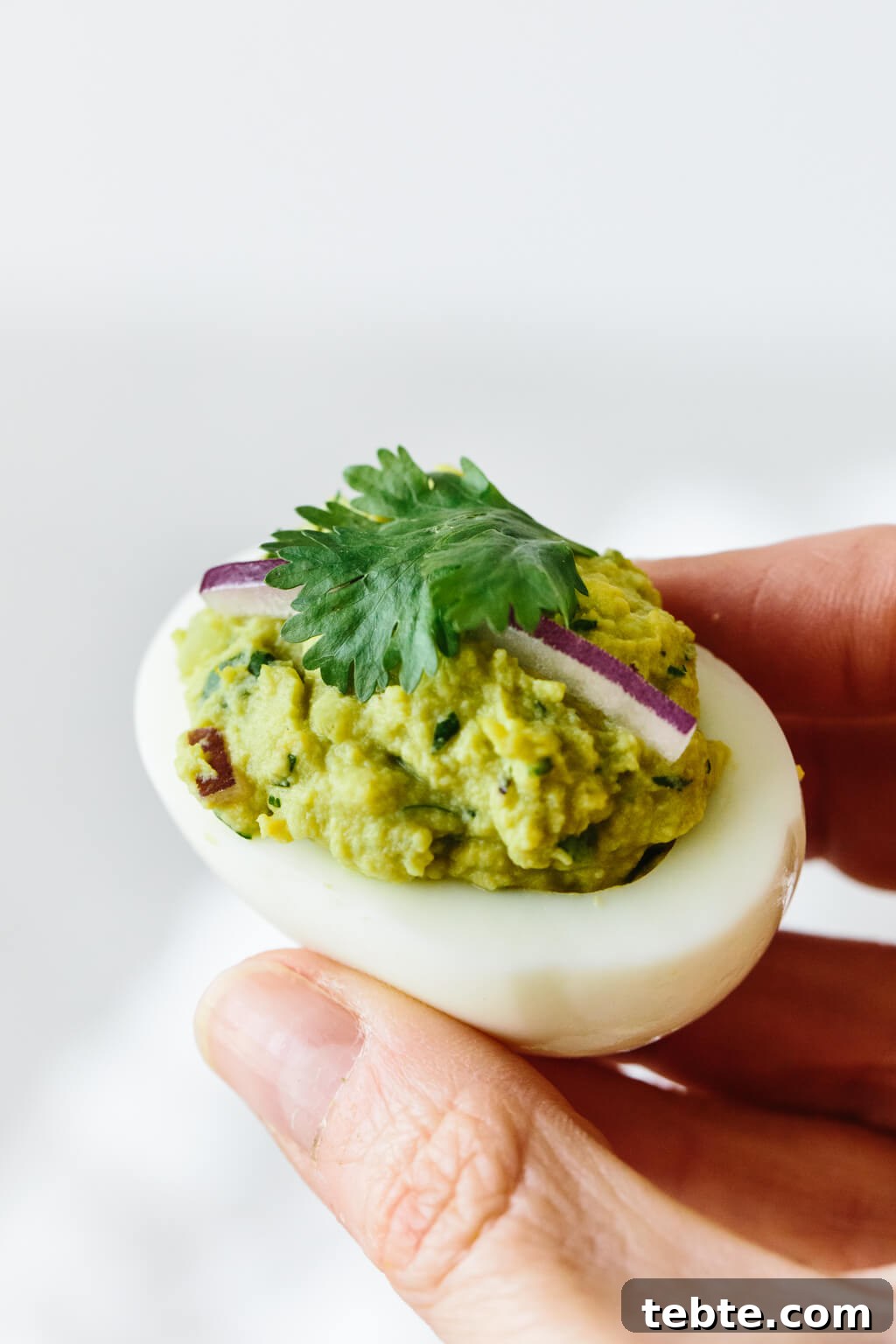 Close up photo of hand holding avocado deviled eggs.