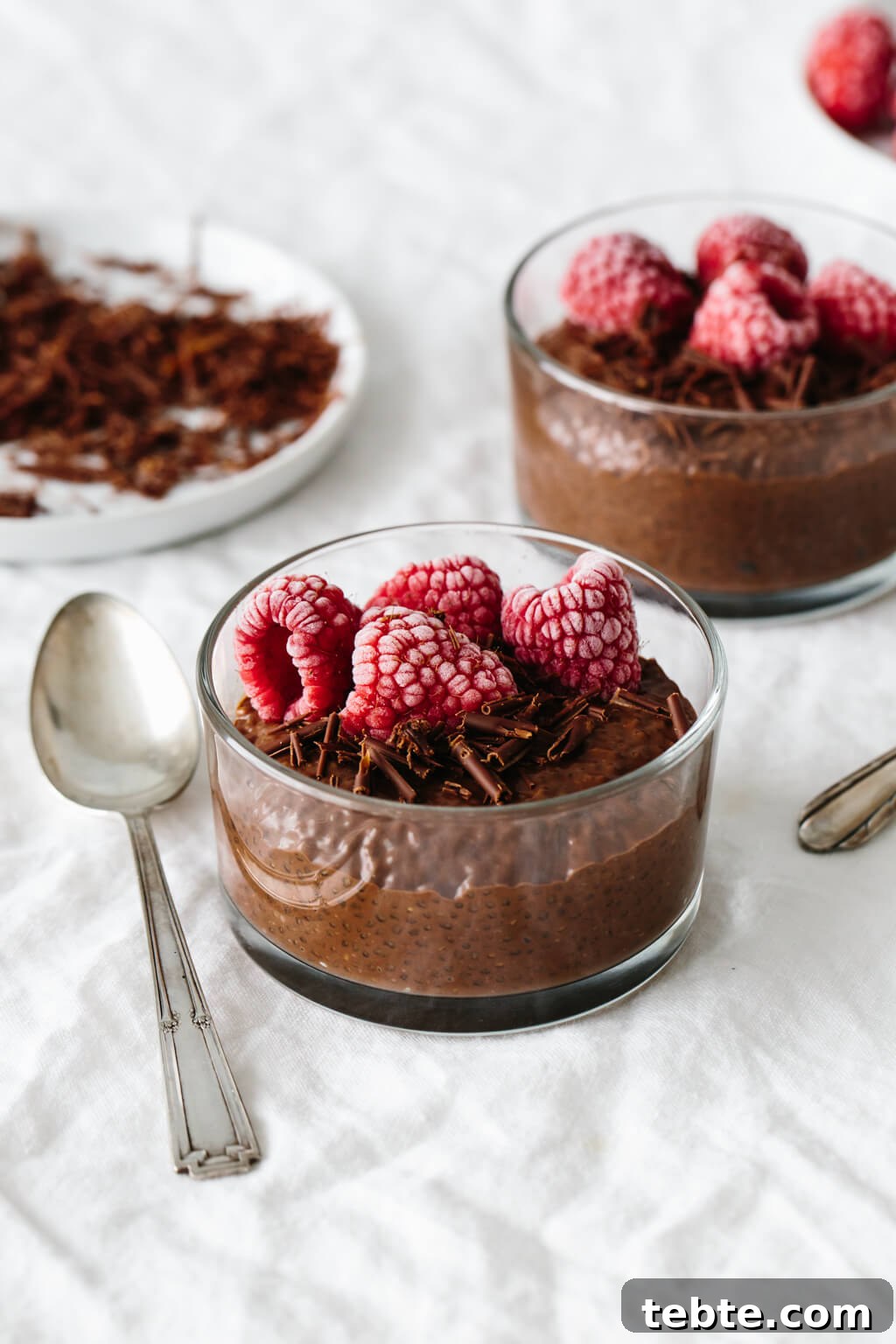 Chocolate chia pudding in a dessert glass with frozen, frosted raspberries on top.
