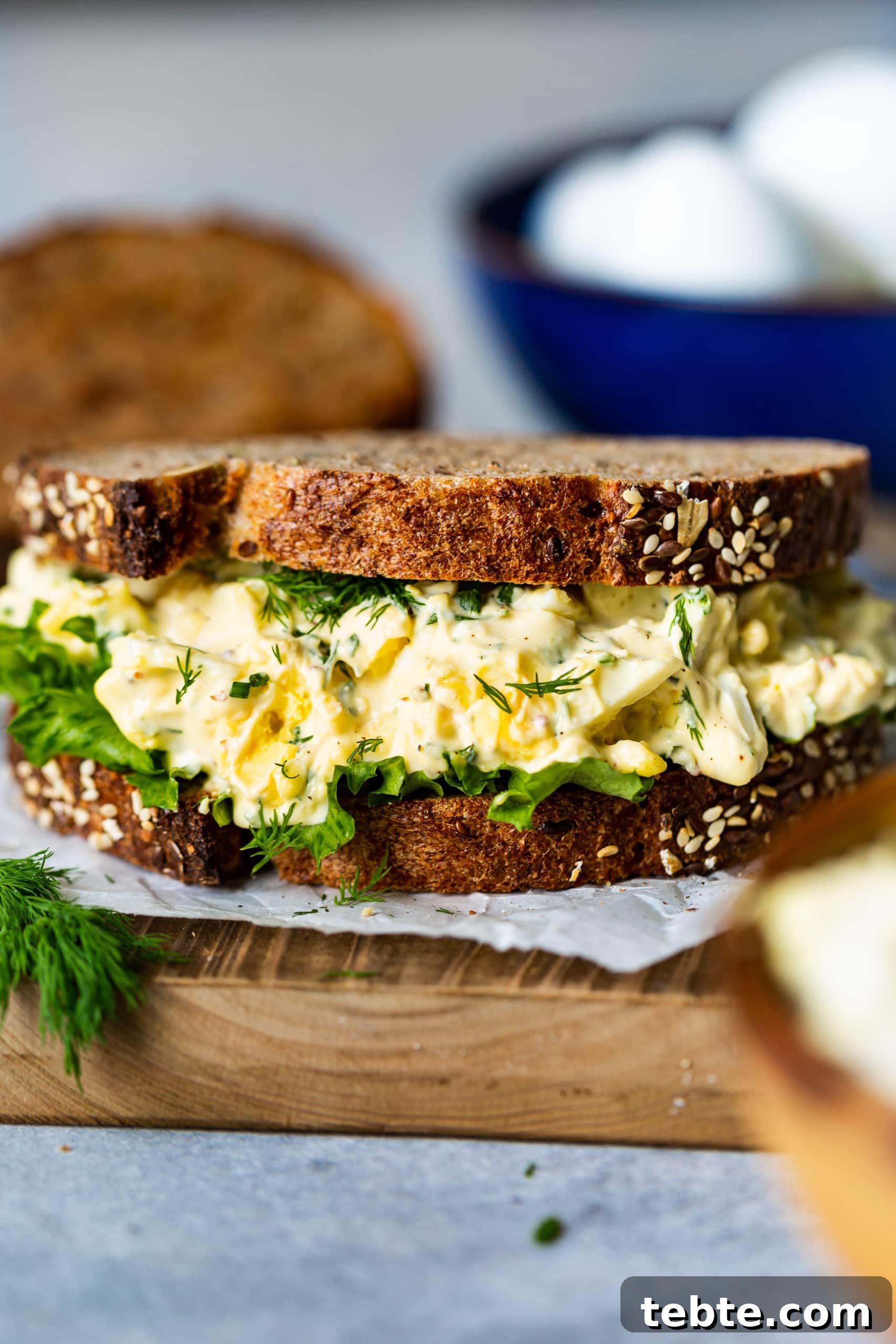 The BEST Egg Salad Sandwich Recipe a photo of an egg salad sandwich piled high with egg salad filling, a piece of lettuce all between two slices of toasted 7 grain bread.