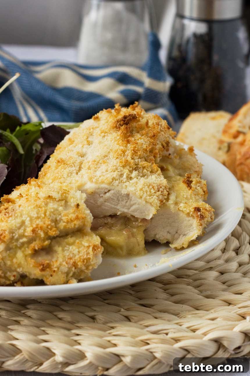 Crispy Baked Chicken Stuffed with Ham and Melted Cheese 2 Crispy baked cheese and ham stuffed chicken on a white plate and wicker place mat with a tea towel behind.