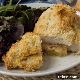 Crispy Baked Chicken Stuffed with Ham and Melted Cheese 5 A crispy cheese and ham stuffed chicken breast on a white plate with salad.