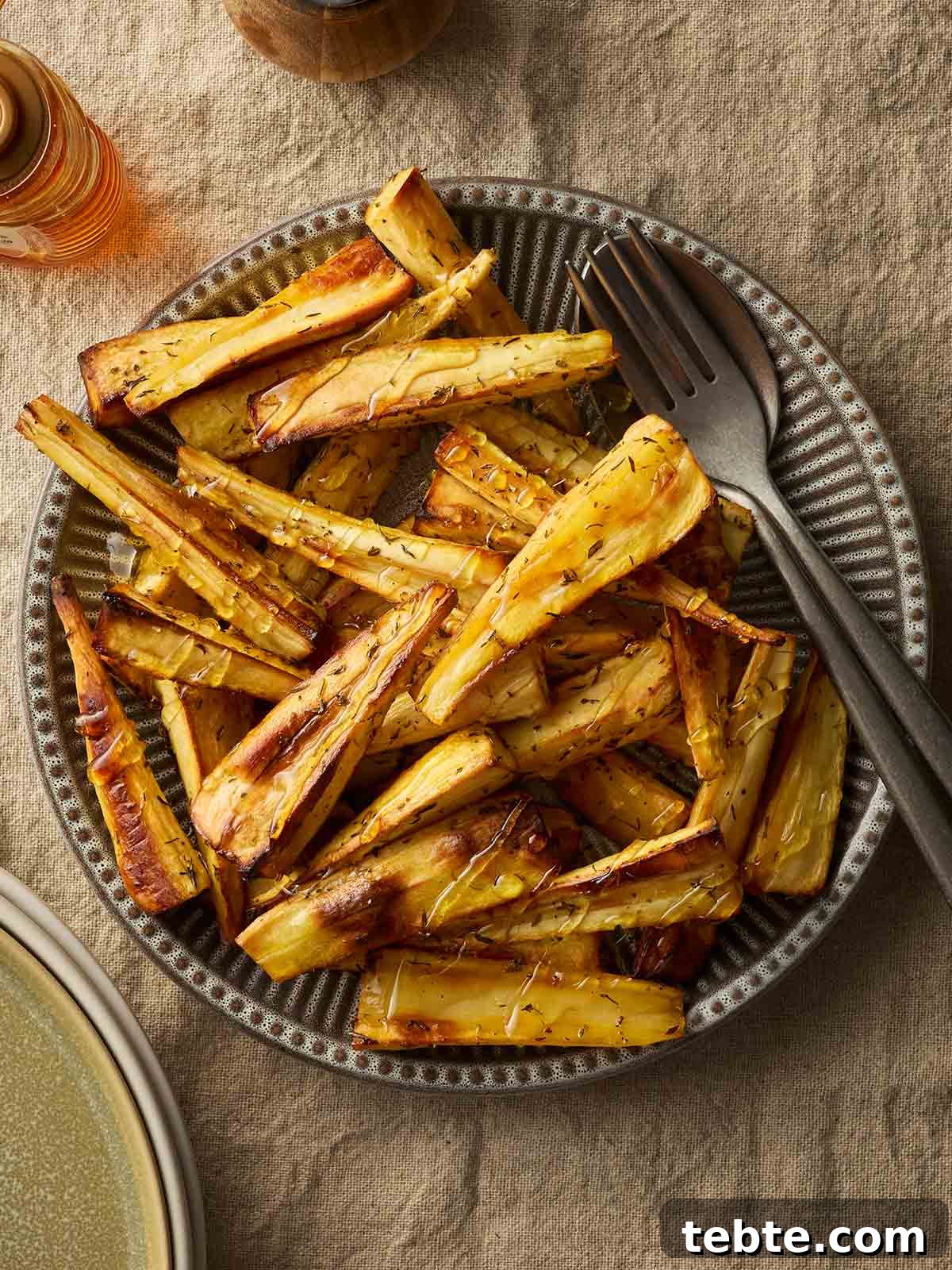 Crispy Roasted Parsnips with Honey and Rosemary 2 A bowl filled with roast parsnips with a fork and knife in.
