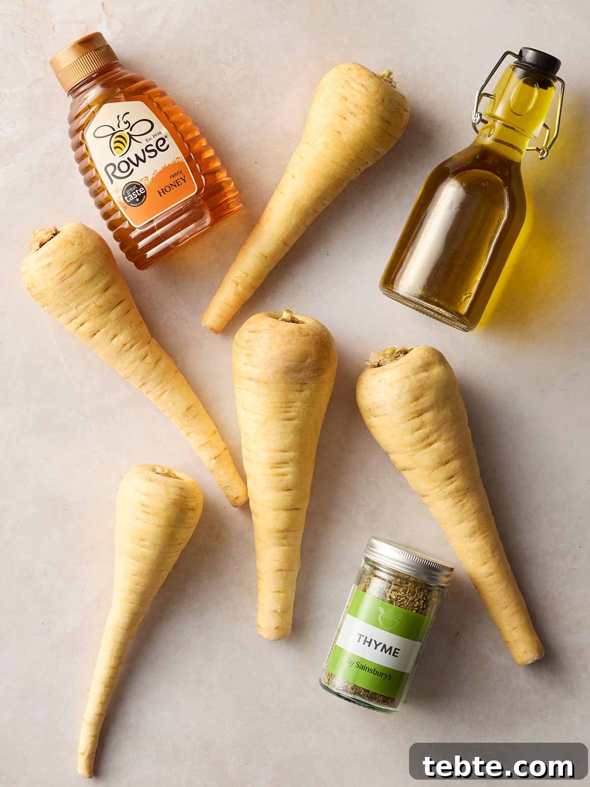 Crispy Roasted Parsnips with Honey and Rosemary 5 A white surface with parsnips, oil, honey and thyme laying on it.