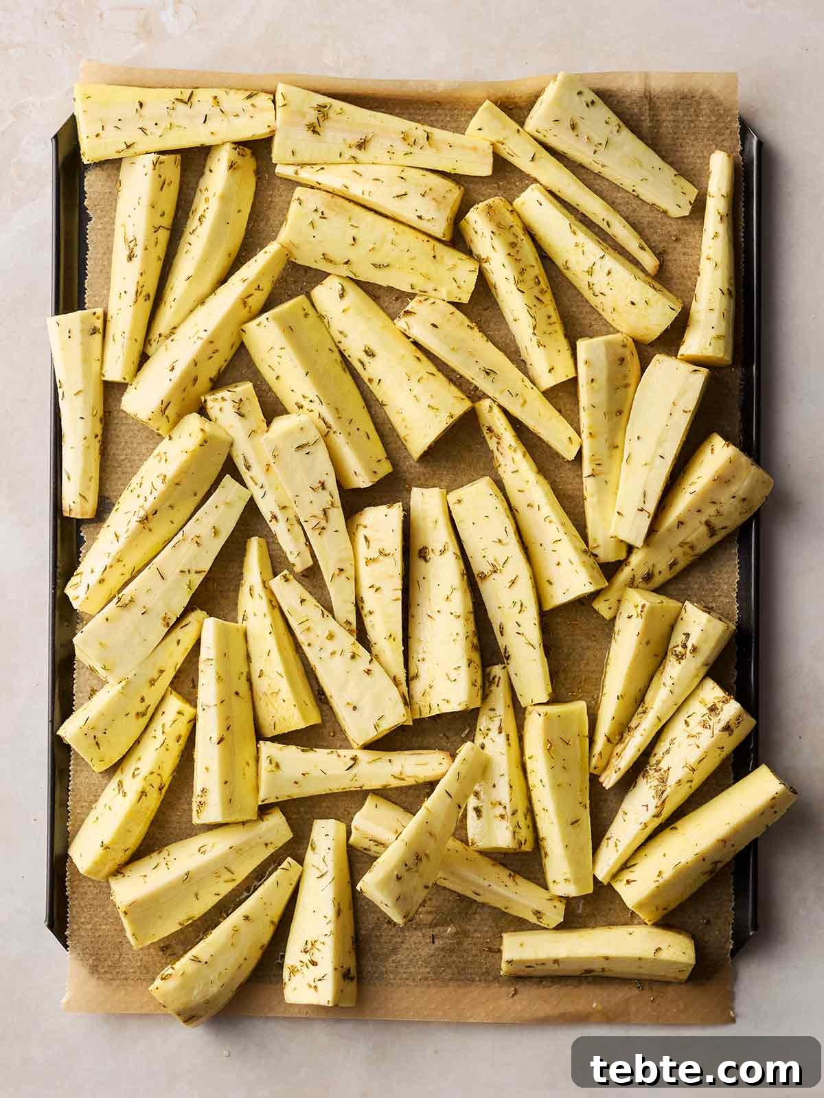Crispy Roasted Parsnips with Honey and Rosemary 7 A lined baking tray on a white surface, with chopped and coated parsnips ready to roast.