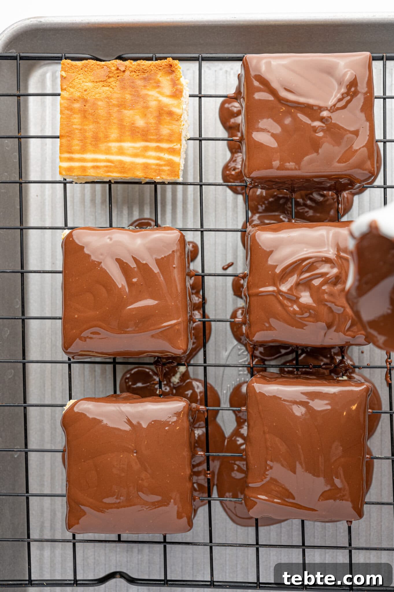 Square pieces of keto cheesecake bites being coated with melted milk chocolate.  