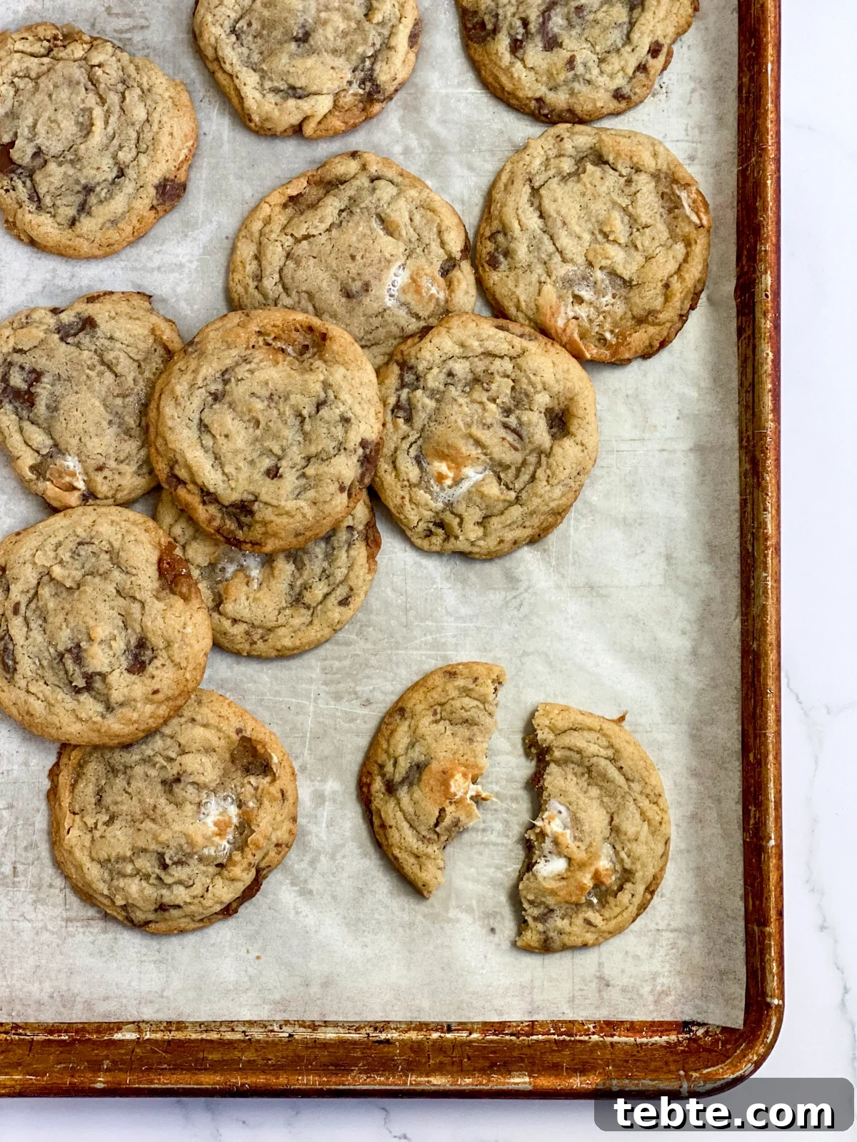 Chewy Chocolate Chip Cookies with Gooey Marshmallow Filling 11 a bunch of chocolate chip marshmallow cookies on a cookie sheet with one broken in half.
