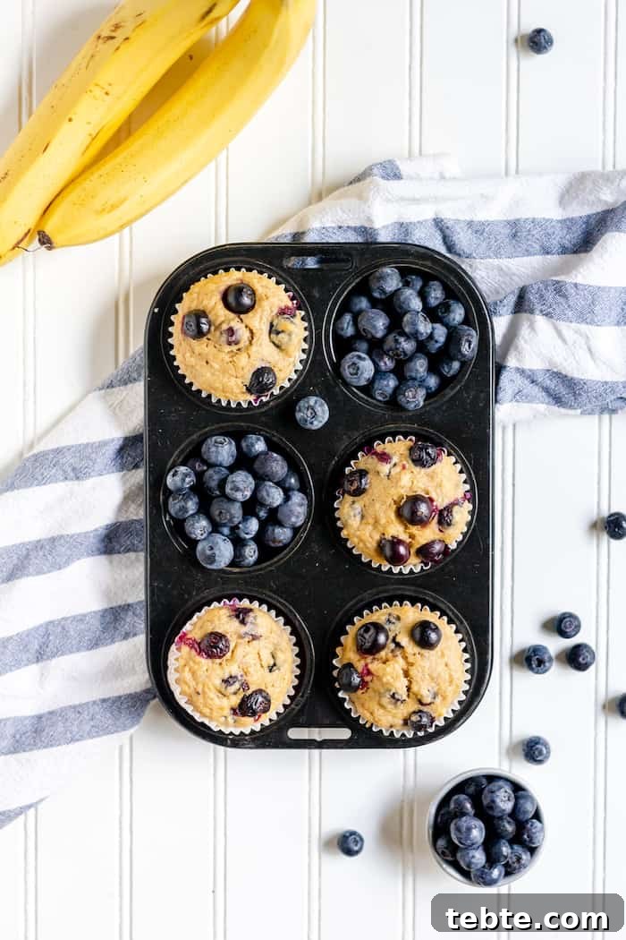 Gluten-Free Blueberry Banana Muffins Recipe for Moist, Tender Muffins 2 Image shows a muffin tin of blueberry muffins and blueberries on a white table