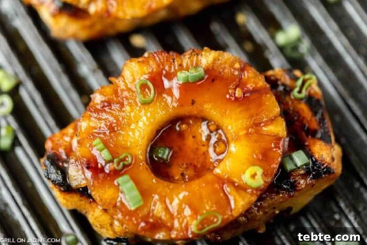 Hawaiian-Style Grilled Pork Chops with Pineapple Glaze 2 Grilled Hawaiian Pork Chops, with grilled pineapple ring topped with chopped green onions, resting on the grill with visible grill marks.