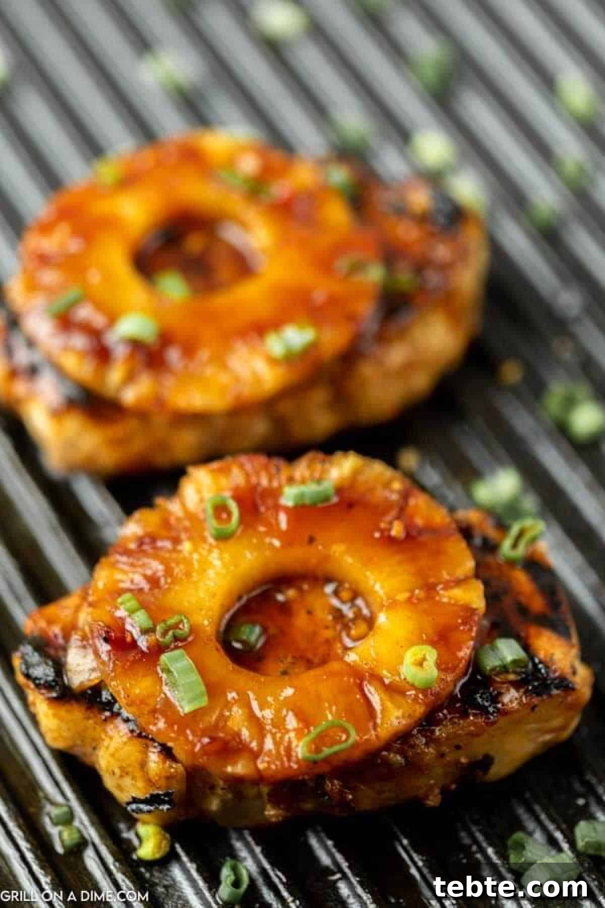Hawaiian-Style Grilled Pork Chops with Pineapple Glaze 9 Two grilled pork chops topped with caramelized pineapple rings and chopped green onions, sitting on a ridged grill pan.