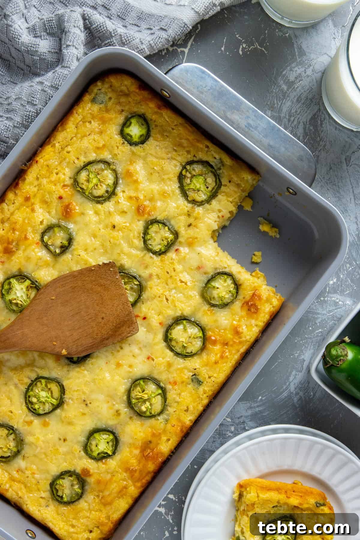 Baked casserole in a baking dish with one serving removed.  One serving on a white plate.  Wooden spoon resting on top of the casserole.