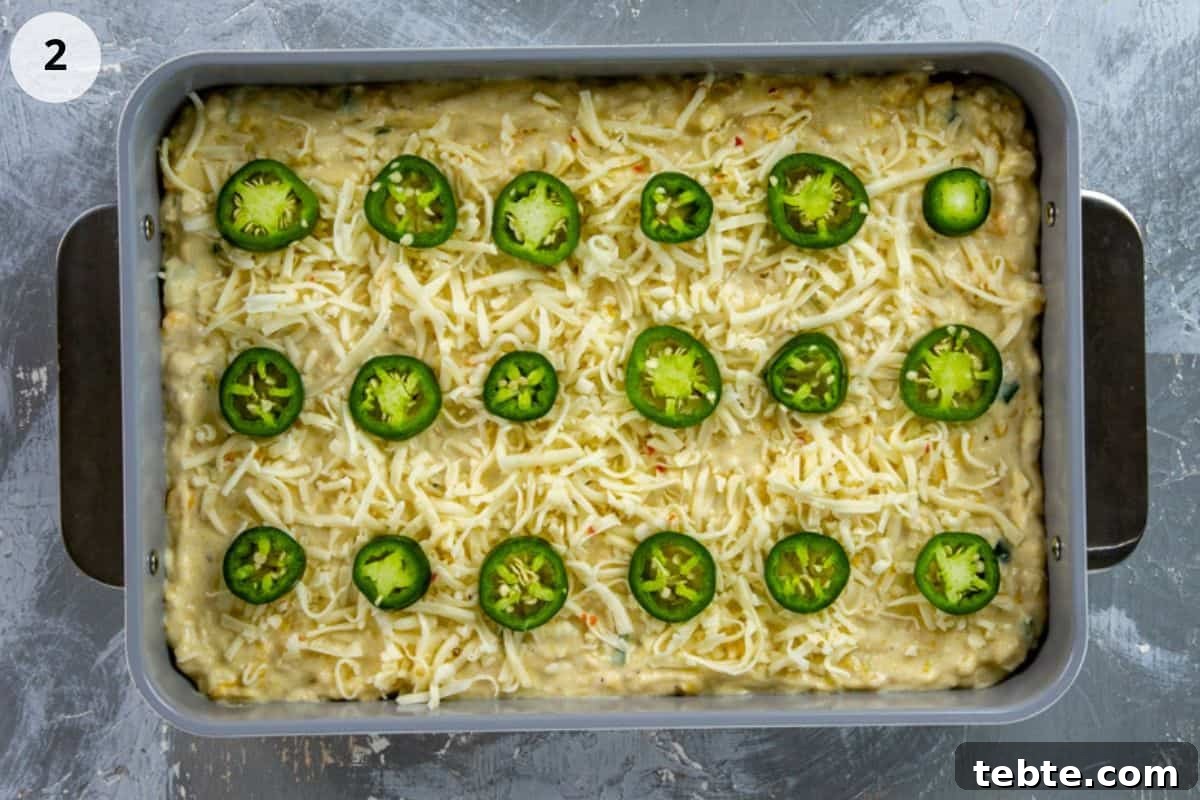 Batter spread into a 9-inch by 13-inch pan. Then sprinkled with shredded pepper jack cheese and fresh jalapeno slices.