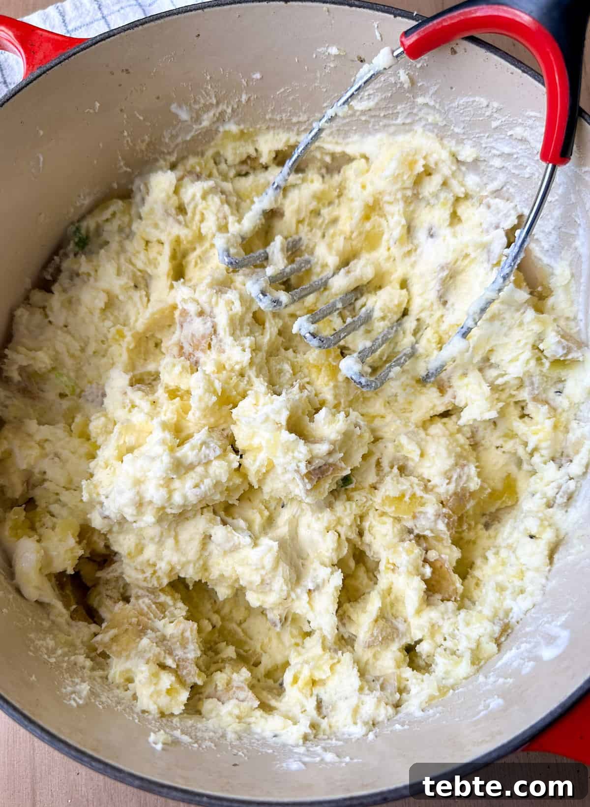 Twice-Baked Potato Casserole: Loaded Mashed Potato Bake 5 Mashed potatoes in a pot with a potato masher.