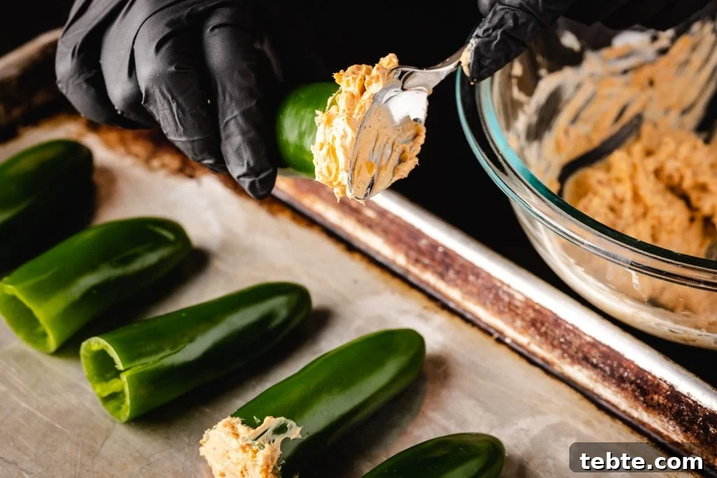 Smoky Bacon-Wrapped Armadillo Eggs: Juicy Jalapeño Poppers with Cream Cheese 3 Jalapenos being stuffed with a cream cheese filling.
