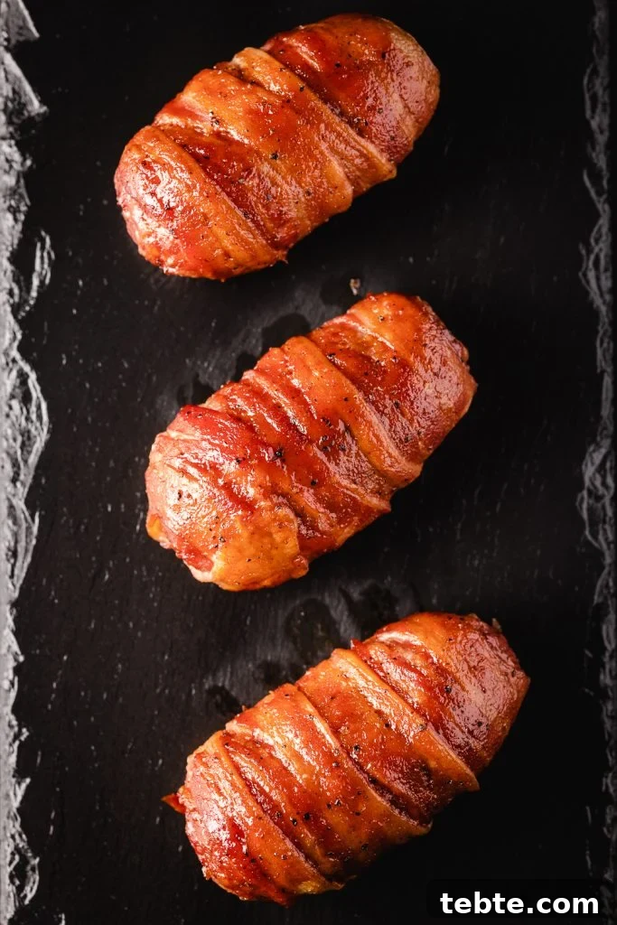 Smoky Bacon-Wrapped Armadillo Eggs: Juicy Jalapeño Poppers with Cream Cheese 6 Three bacon wrapped armadillo eggs on a black serving platter.