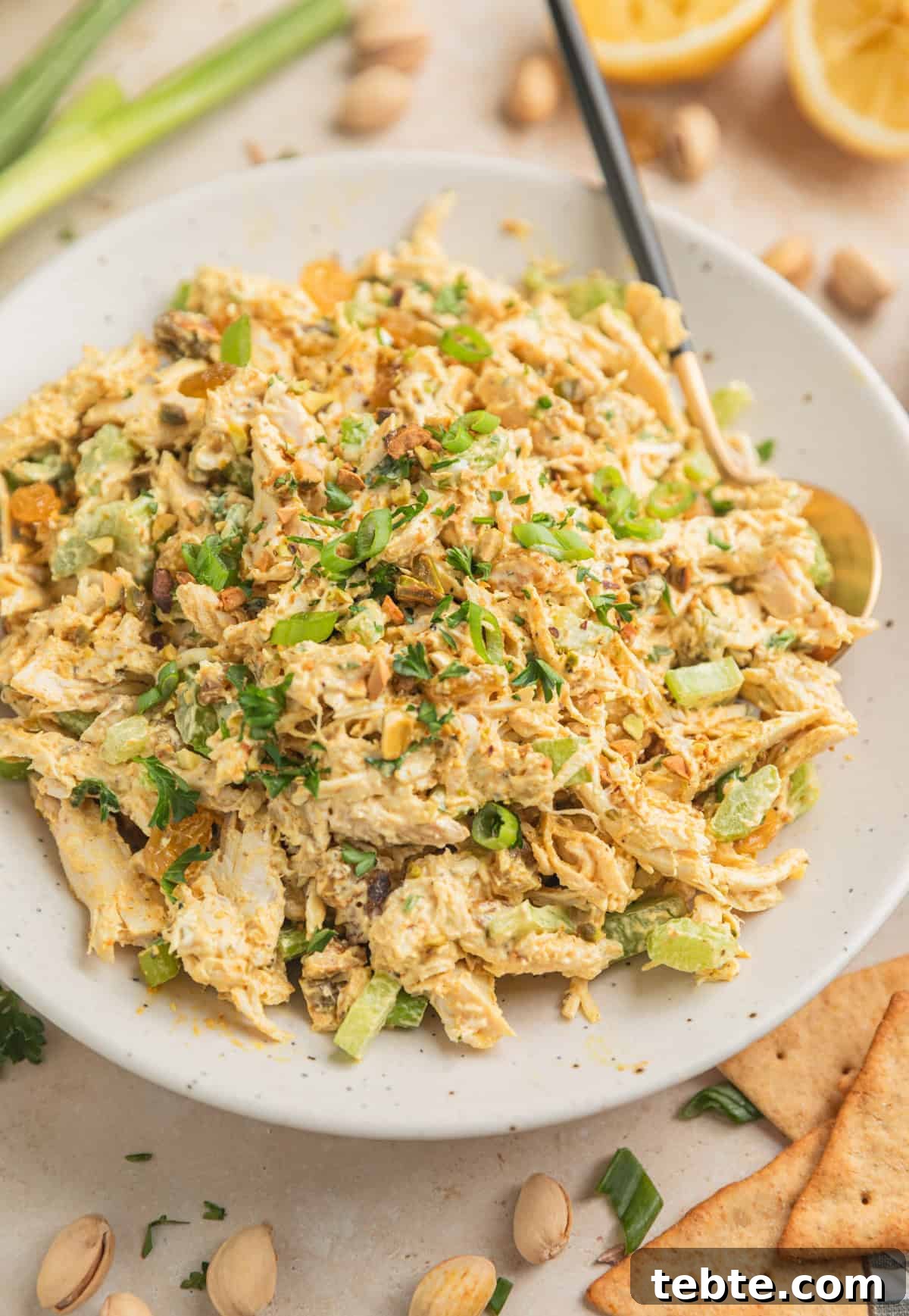 Creamy Curry Chicken Salad Recipe with Crunchy Apples and Almonds 2 Curry chicken salad in dish with spoon topped with chopped green onion, chopped pistachios and parsley.