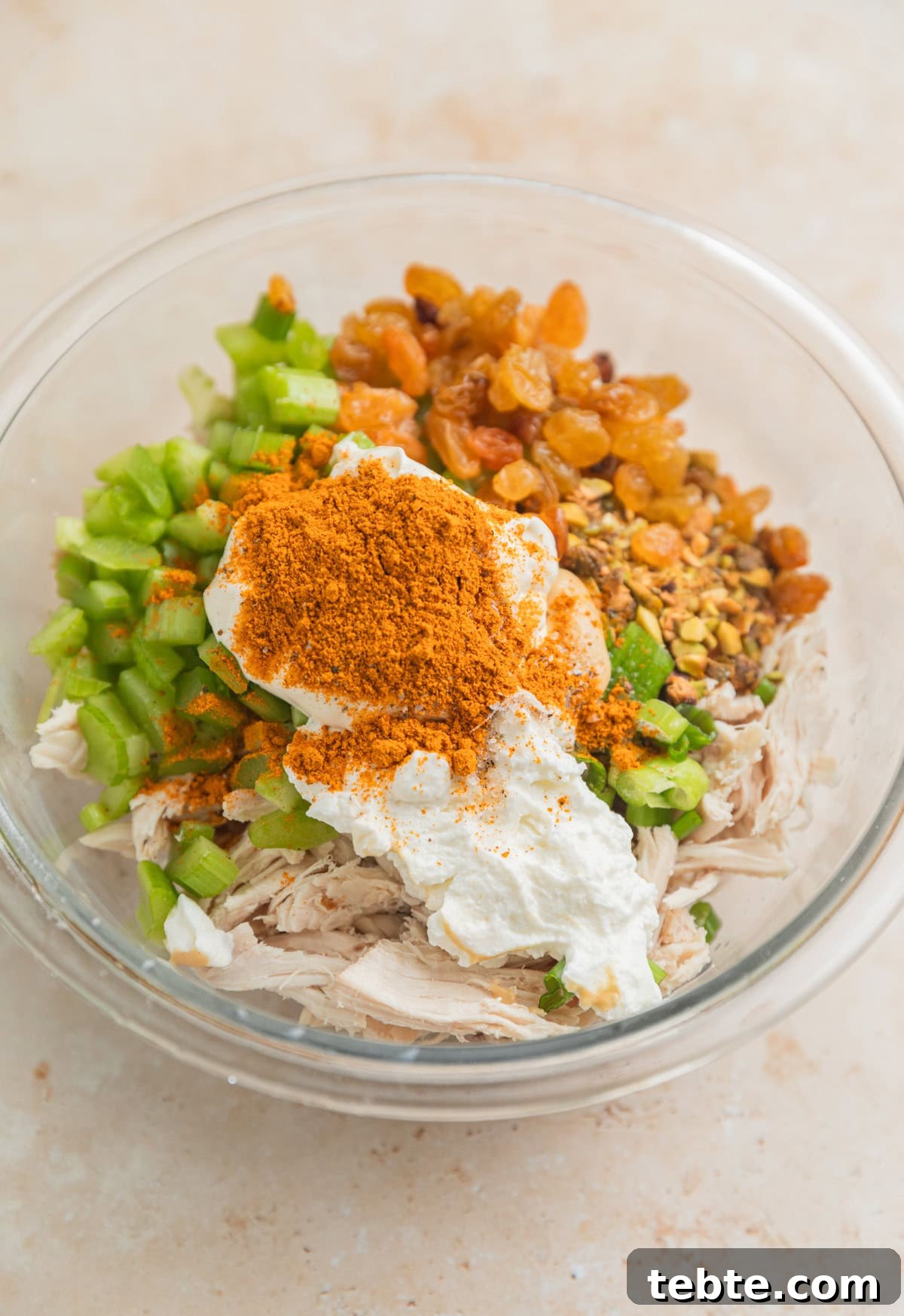Creamy Curry Chicken Salad Recipe with Crunchy Apples and Almonds 4 Shredded chicken, celery, golden raisins, curry powder and other chicken salad ingredients in glass bowl.