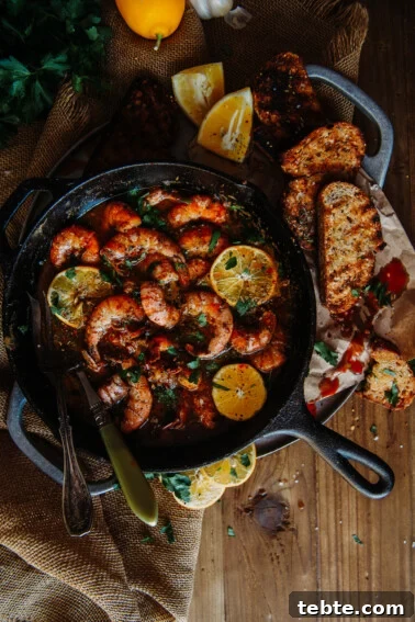 Crispy Halloumi Shrimp Saganaki with Tomato and Feta 14 cast iron skillet filled with spicy sauce, jumbo shrimp, lemons and bread on the side for dipping