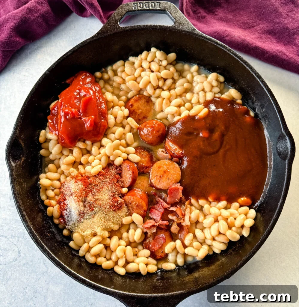 Classic Homemade Pork and Beans Recipe for Comforting Meals 8 kidney beans with ketchup, BBQ sauce, BBQ rub spices, bacon, and sausage in a cast iron skillet
