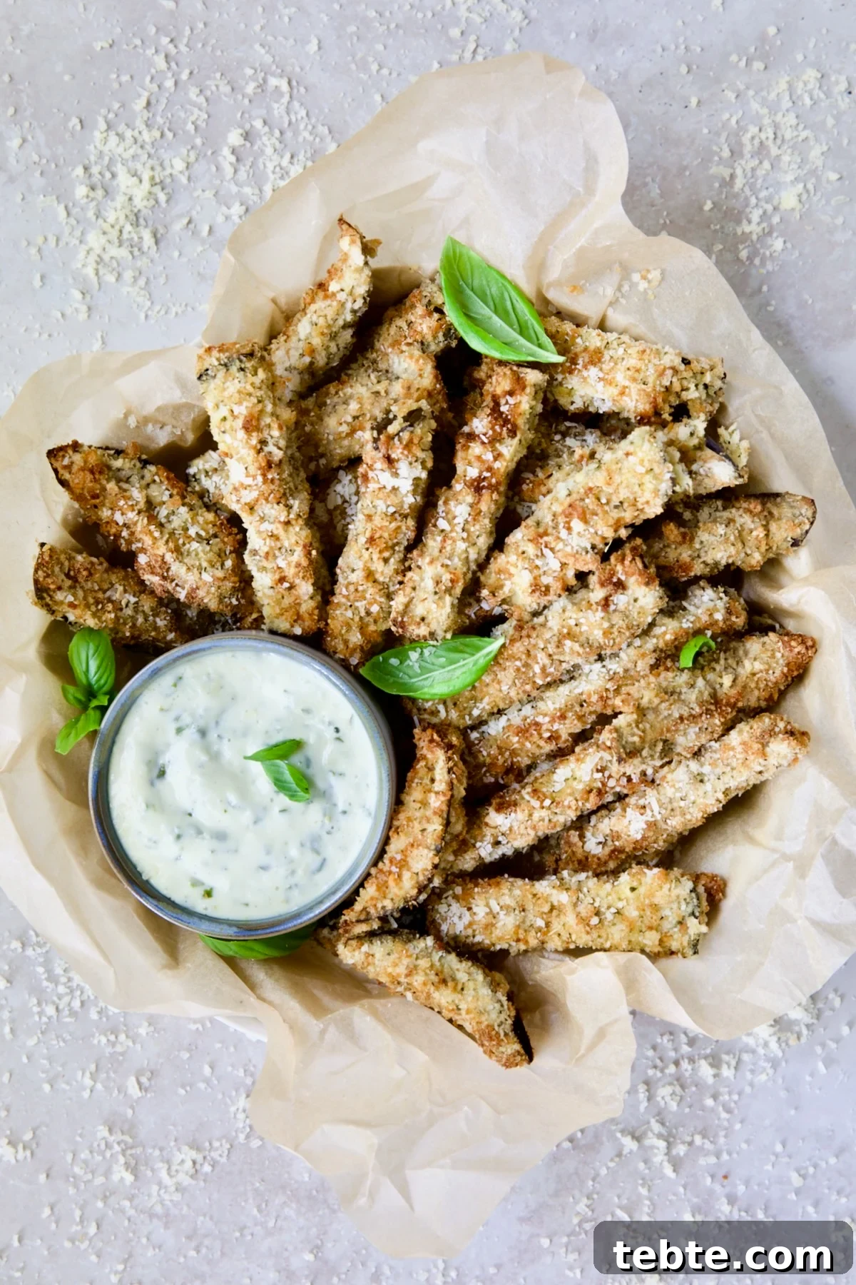 Crispy Air Fryer Eggplant Fries with Garlic Parmesan Dip 2 Air Fryer Eggplant Fries with Garlic Basil Aioli in basket with parmesan cheese and fresh basil leaves.