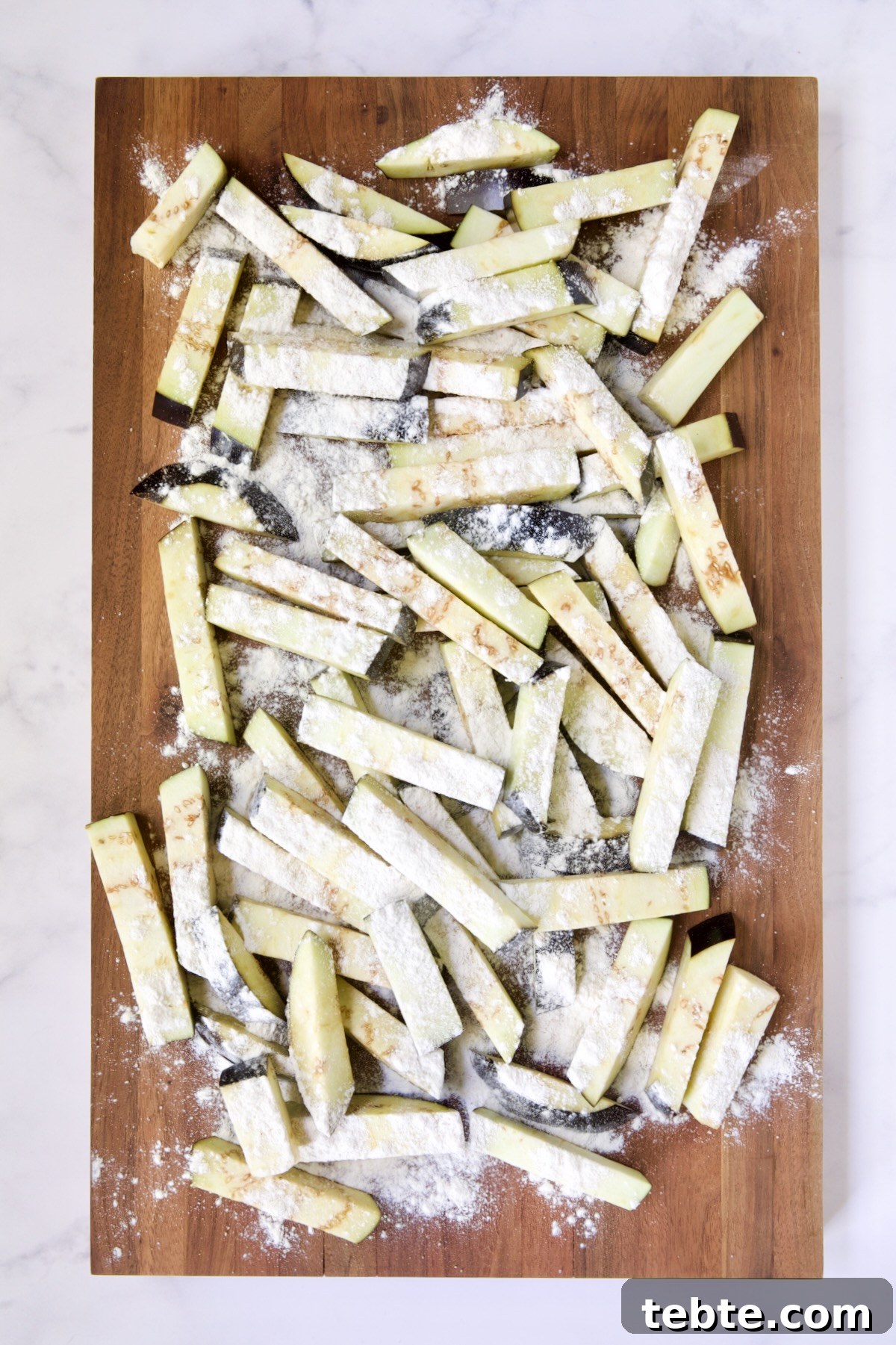 Crispy Air Fryer Eggplant Fries with Garlic Parmesan Dip 11 Eggplant fries on wood cutting board dusted with all-purpose flour.