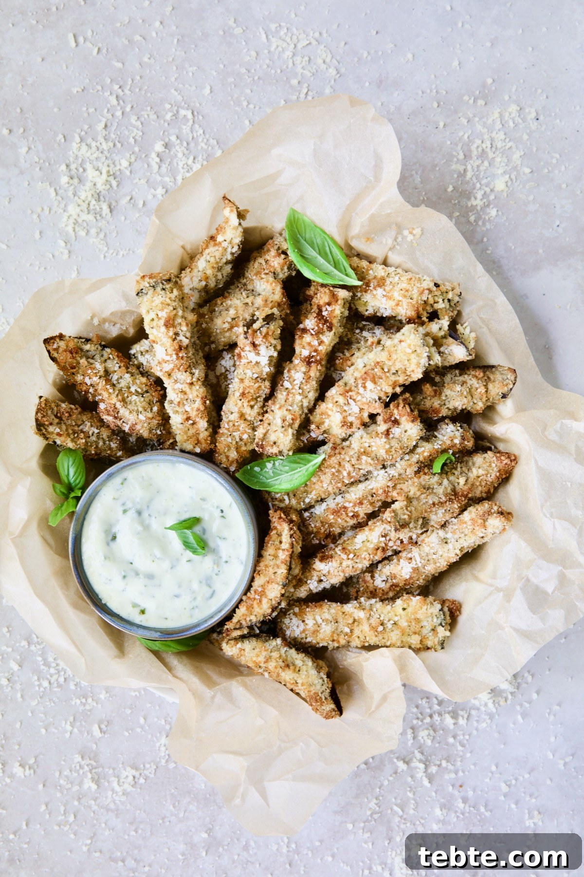 Crispy Air Fryer Eggplant Fries with Garlic Parmesan Dip 17 Air Fryer Eggplant Fries with Garlic Basil Aioli in parchment paper lined basket with Parmesan cheese scattered about.