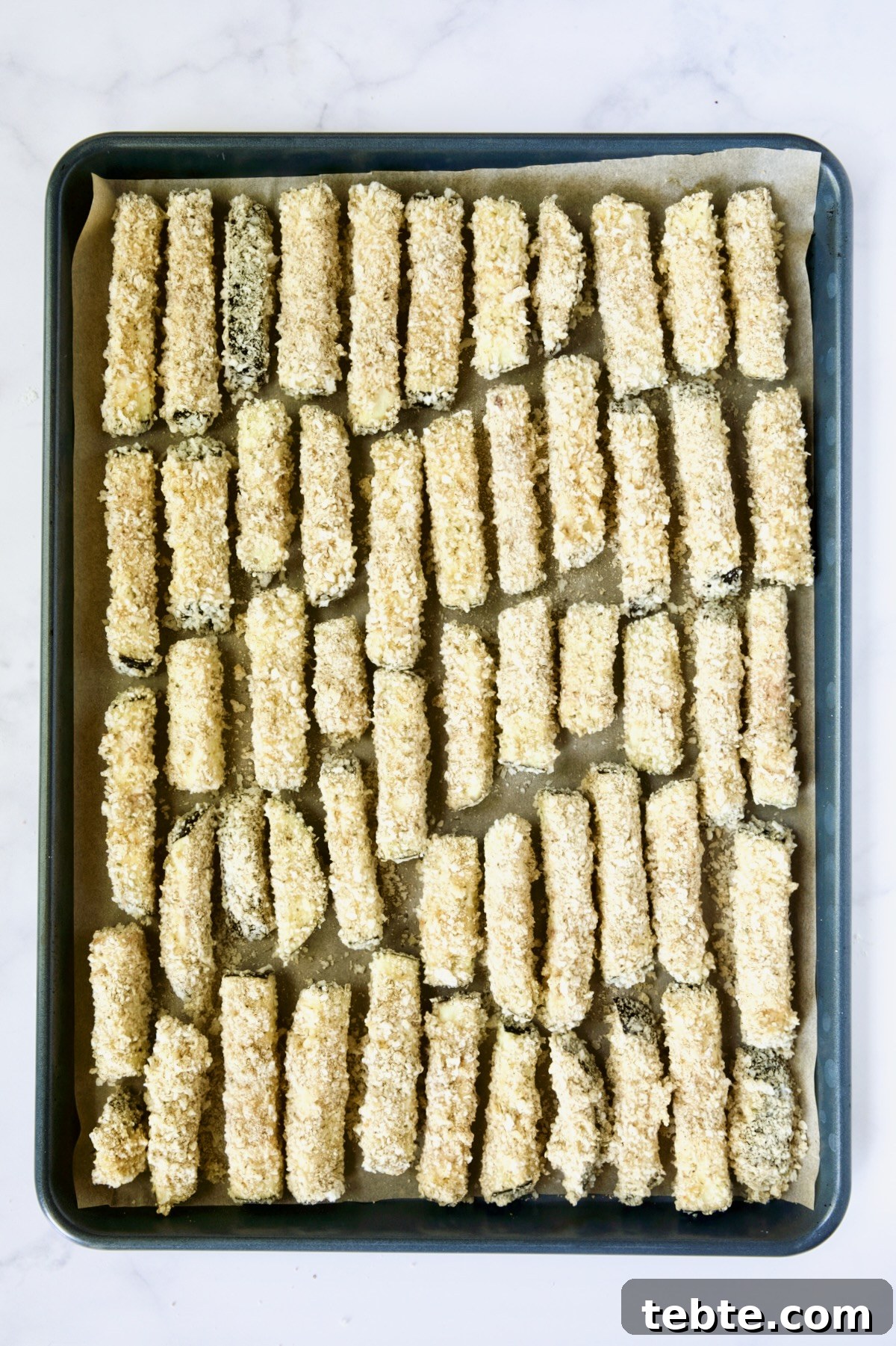 Crispy Air Fryer Eggplant Fries with Garlic Parmesan Dip 19 Breaded eggplant fries on parchment paper-lined rimmed baking sheet.