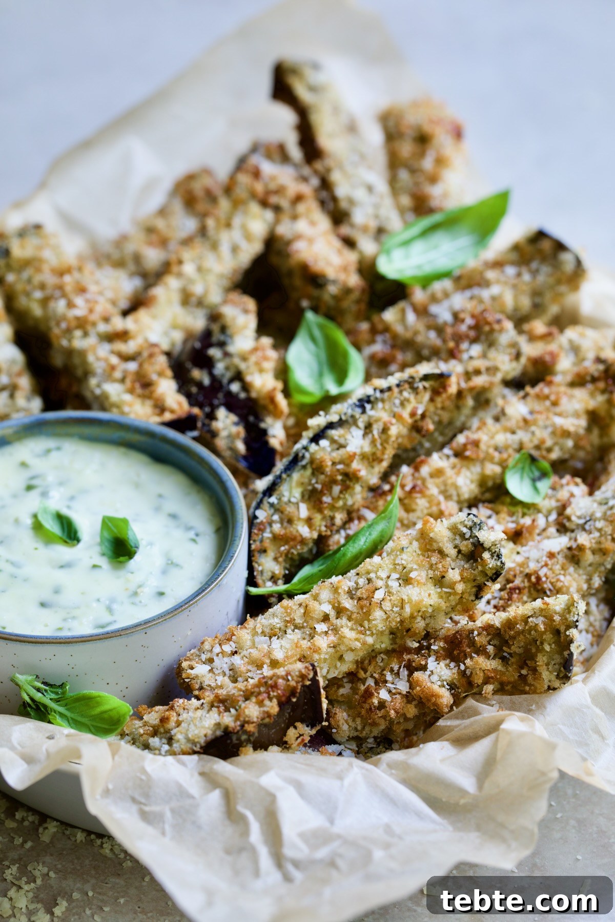 Crispy Air Fryer Eggplant Fries with Garlic Parmesan Dip 3 Air Fryer Eggplant Fries with Garlic Basil Aioli in parchment lined basket garnished with fresh basil.