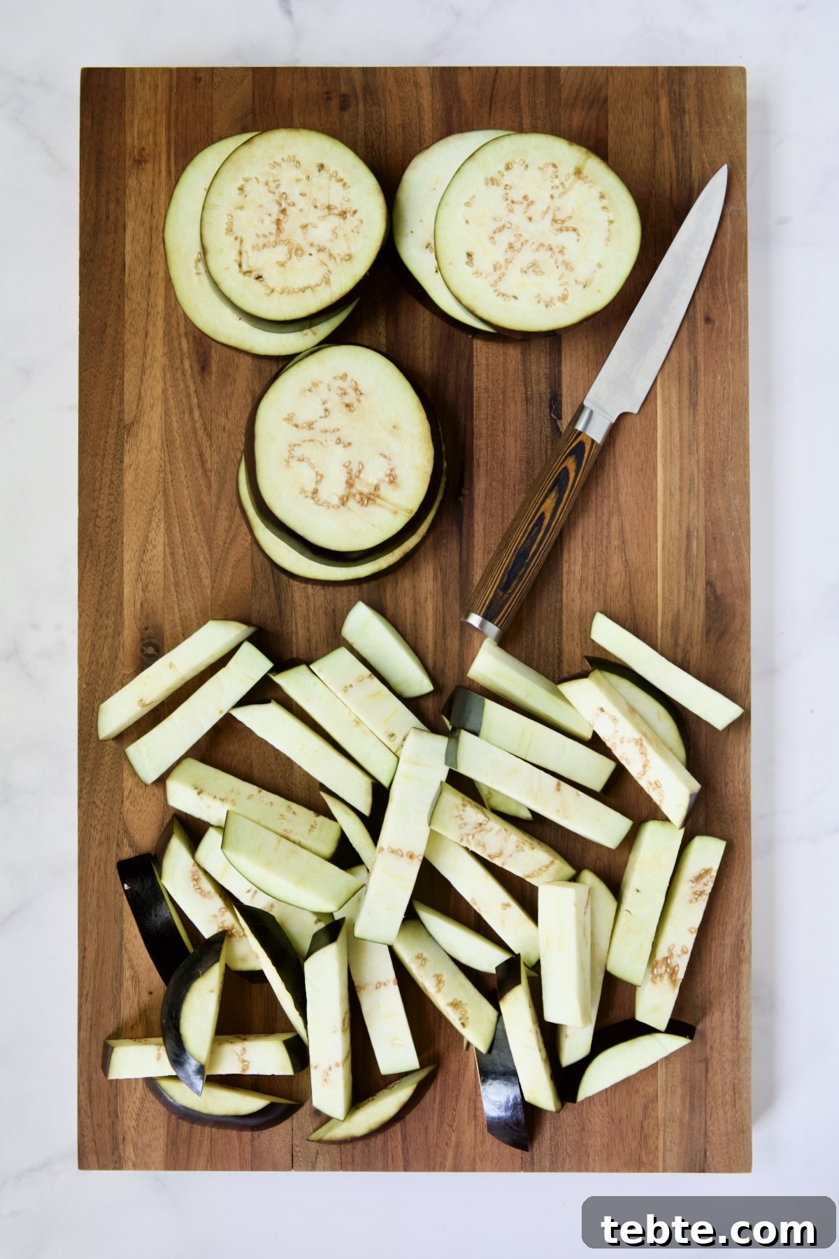 Crispy Air Fryer Eggplant Fries with Garlic Parmesan Dip 10 Eggplant rounds and fries on wood cutting board with knife.