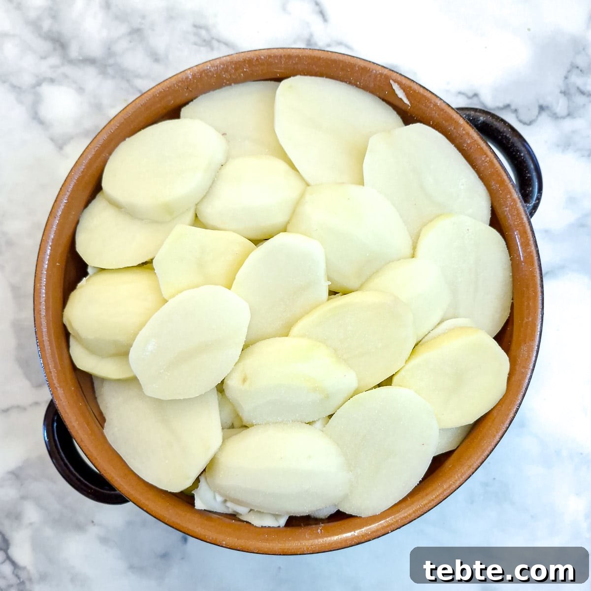 A final layer of thickly sliced potatoes on top.