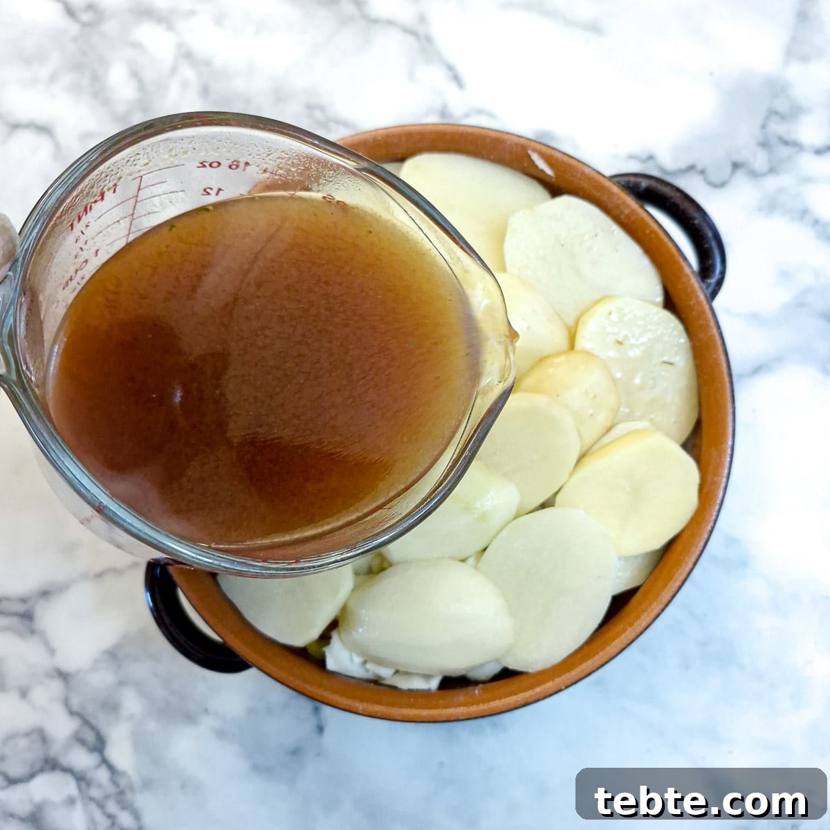A glass jug of stock being poured into the casserole.