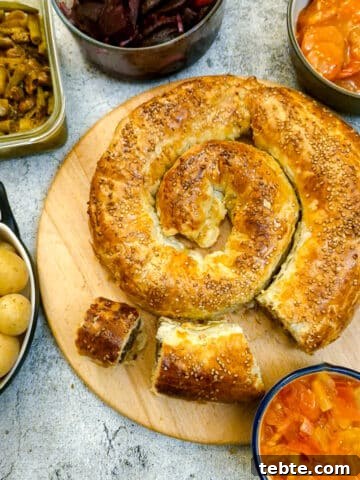 A boerewors puff pastry spiral on a wooden board surrounded by a selection of salads.