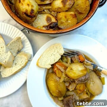 A deep white plate, filled with lamb potjie, with a slice of crusty bread on the side.