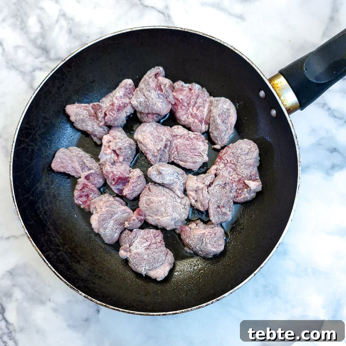 Pieces of flour-coated lamb browning in a frying pan.