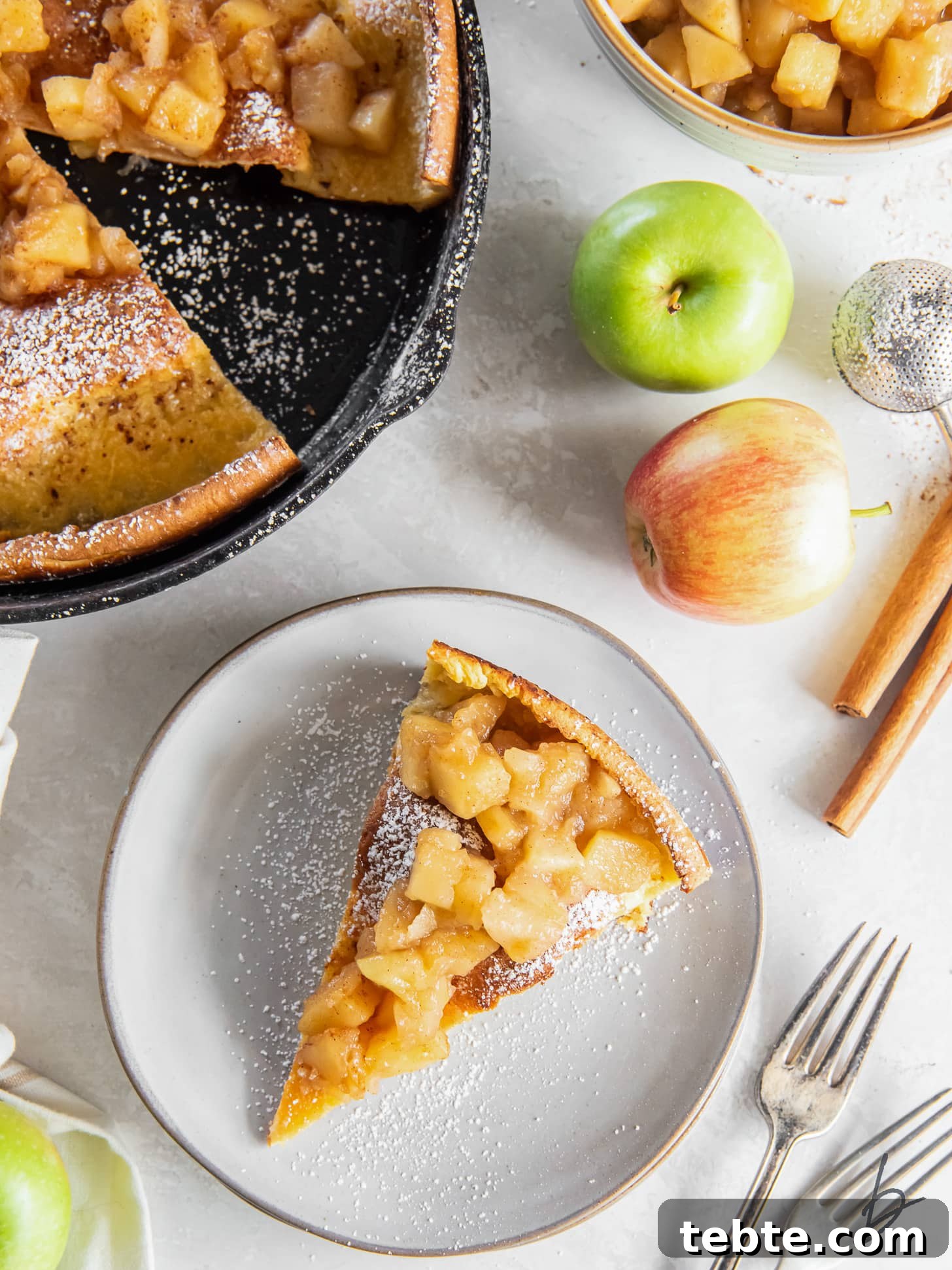 Classic Apple Dutch Baby Pancake Recipe for Brunch 6 slice of apple dutch baby on a plate next to fresh apples and cinnamon sticks.