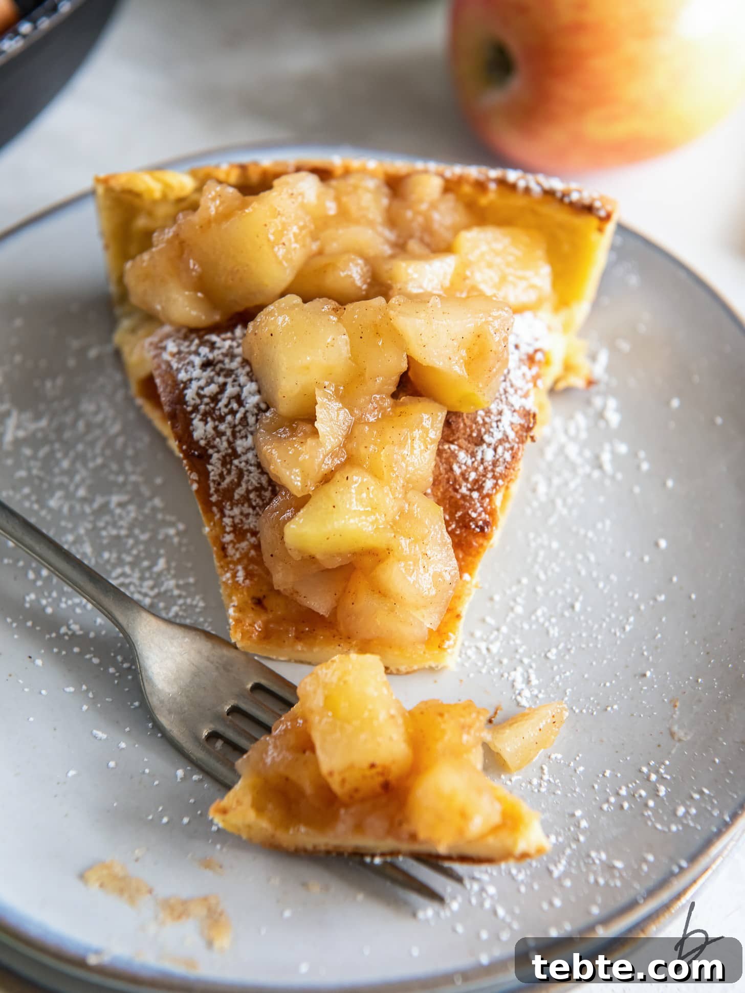 Classic Apple Dutch Baby Pancake Recipe for Brunch 7 fork hoding bite of dutch baby with apples and dusting of pwodered sugar.