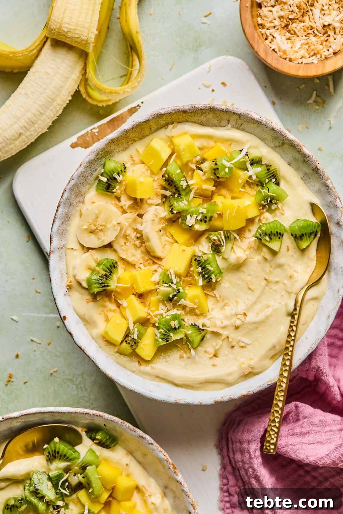 coconut smoothie bowl with toppings on a counter next to a peeled banana and bowl of toasted coconut 