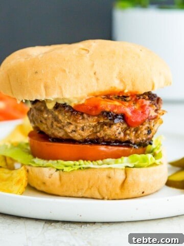 A gluten free burger in a bun with lettuce, tomato and ketchup.