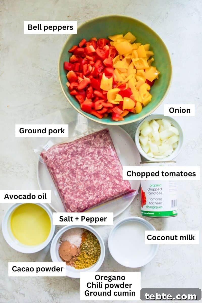 The ingredient needed to make chili in separate bowls including bell peppers, onion, ground pork, tomatoes and spices.