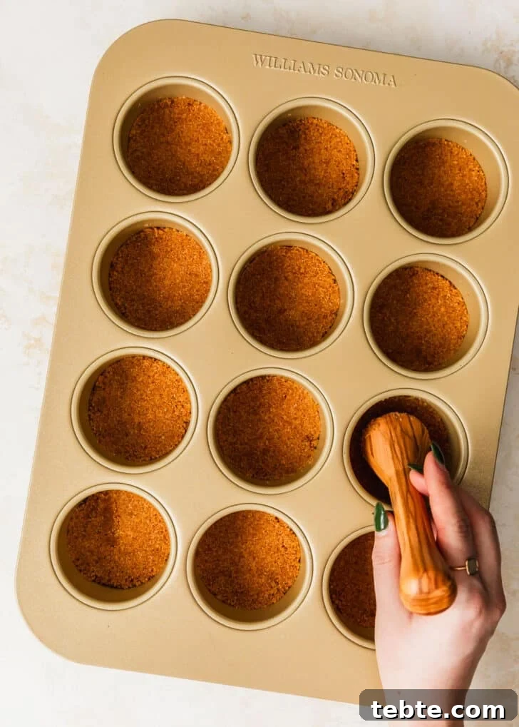 Mini Strawberry Cheesecakes Recipe: Perfect Bite-Sized Treats 8 A hand using a pastry tamper to press graham cracker crust into a mini cheesecake pan.