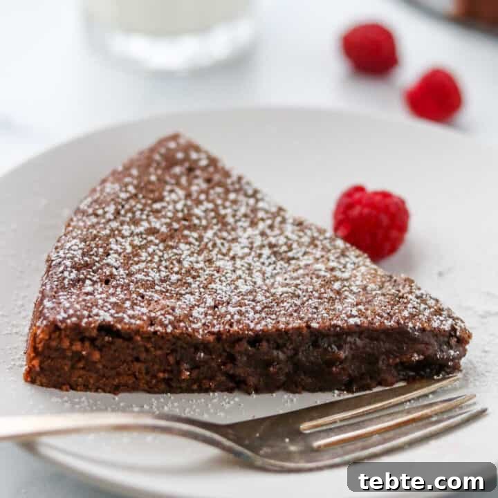 Closeup of a slice of kladdkaka on a plate next to a fork and raspberries.