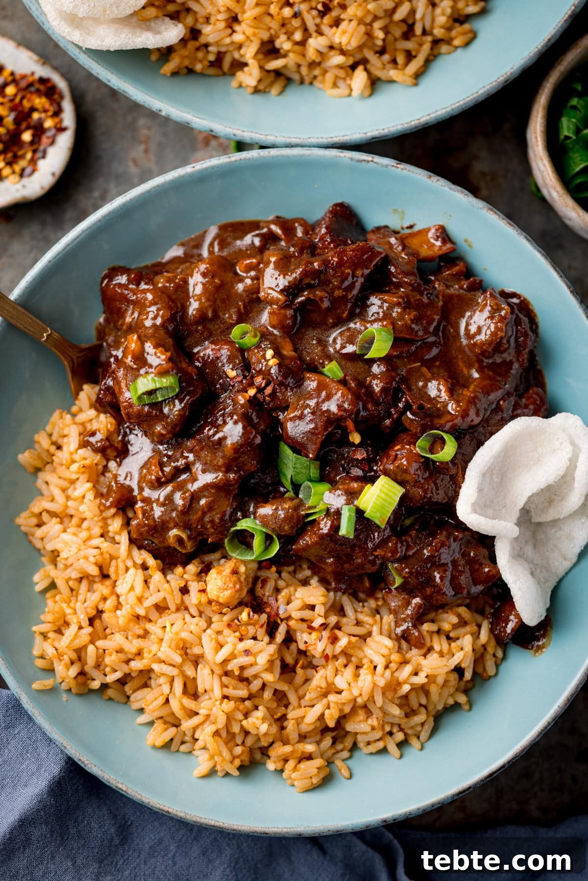 Chinese-Style Beef Curry Recipe: Savory Stir-Fry with Aromatics 5 Chinese beef curry and rice in a blue bowl, garnished with chopped spring onions a couple of prawn crackers. There is a further bowl of curry and accompaniments next to the bowl.