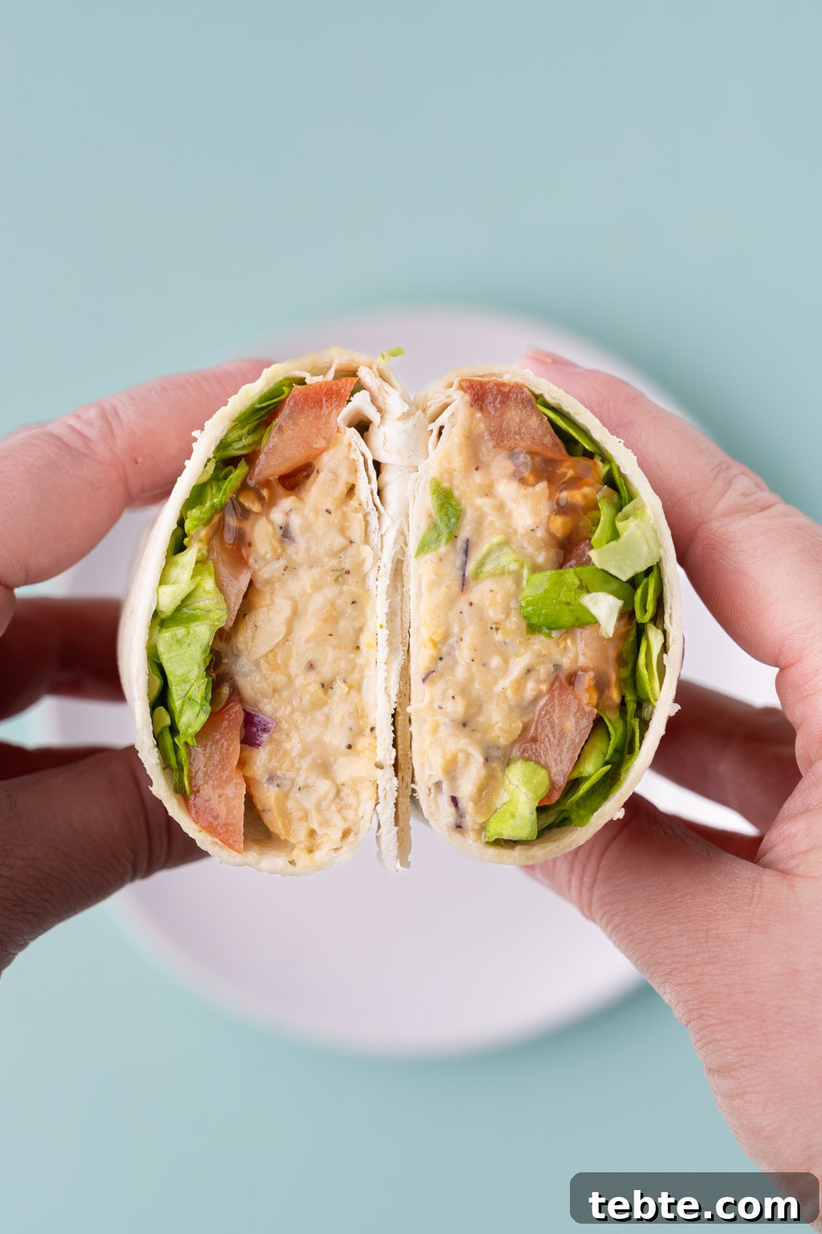10-Minute Chickpea Salad Wrap Recipe for Quick Lunch 2 Lunch wrap with chickpea salad, tomatoes, and lettuce cut in half and held up to the camera to show the inside.