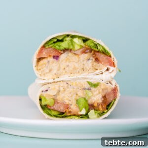 10-Minute Chickpea Salad Wrap Recipe for Quick Lunch 11 Cold chickpea wrap sliced in half and presented on a white plate with two halves stacked on top of one another.
