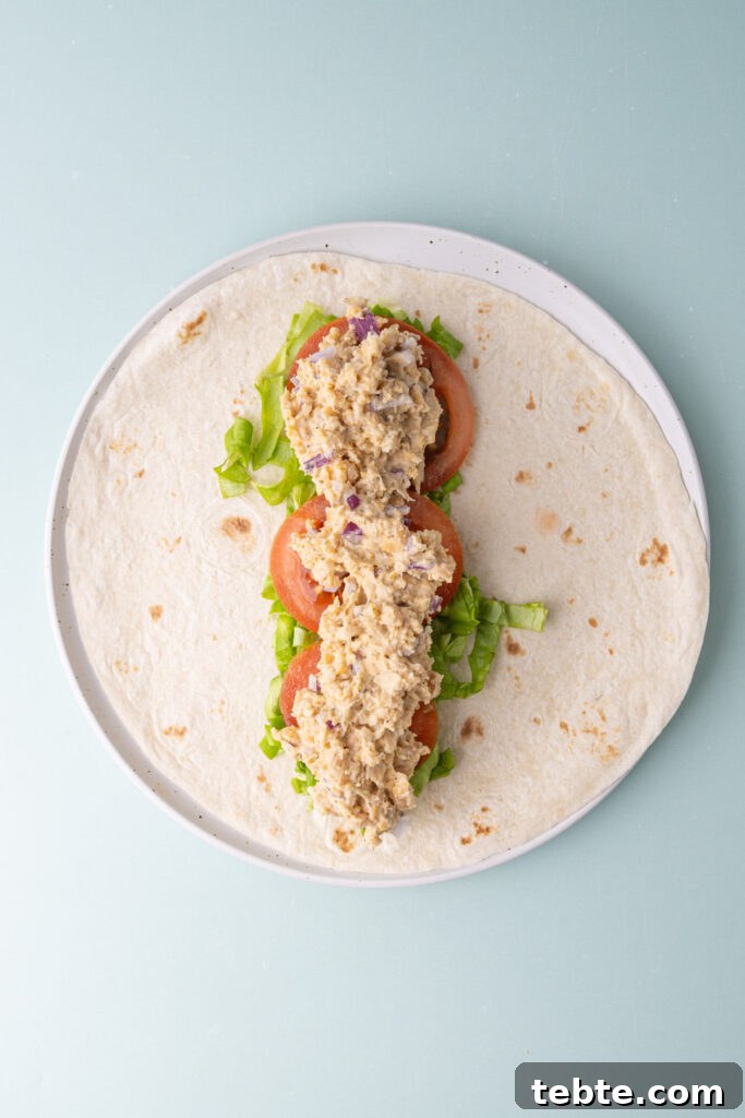 10-Minute Chickpea Salad Wrap Recipe for Quick Lunch 6 Tortilla with chopped lettuce, sliced tomato, and chickpea salad in the center of the tortilla.