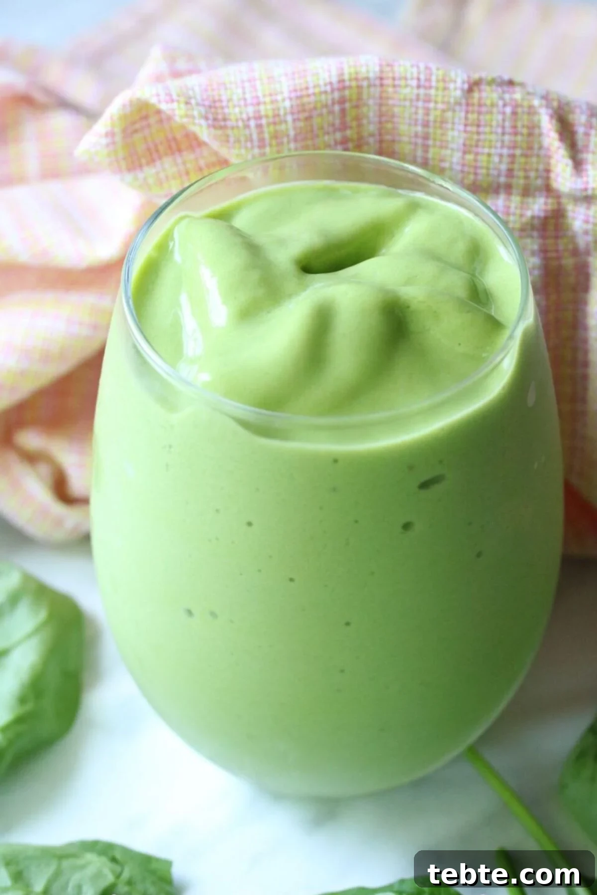 Mango Avocado Smoothie Without Banana — Creamy Tropical Drink 2 Mango green smoothie in a tumbler glass with spinach leaves around it and an orange linen behind it.