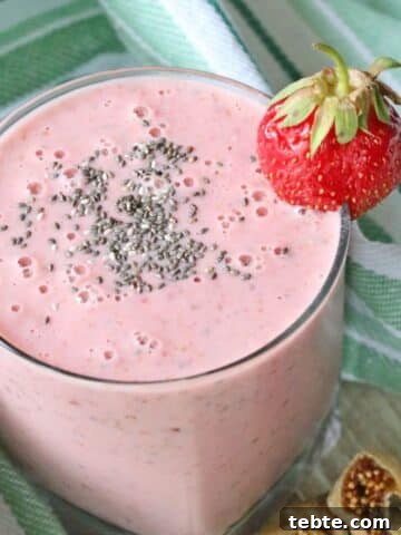Strawberry smoothie in a glass with chia seeds on top and a strawberry on the glass.